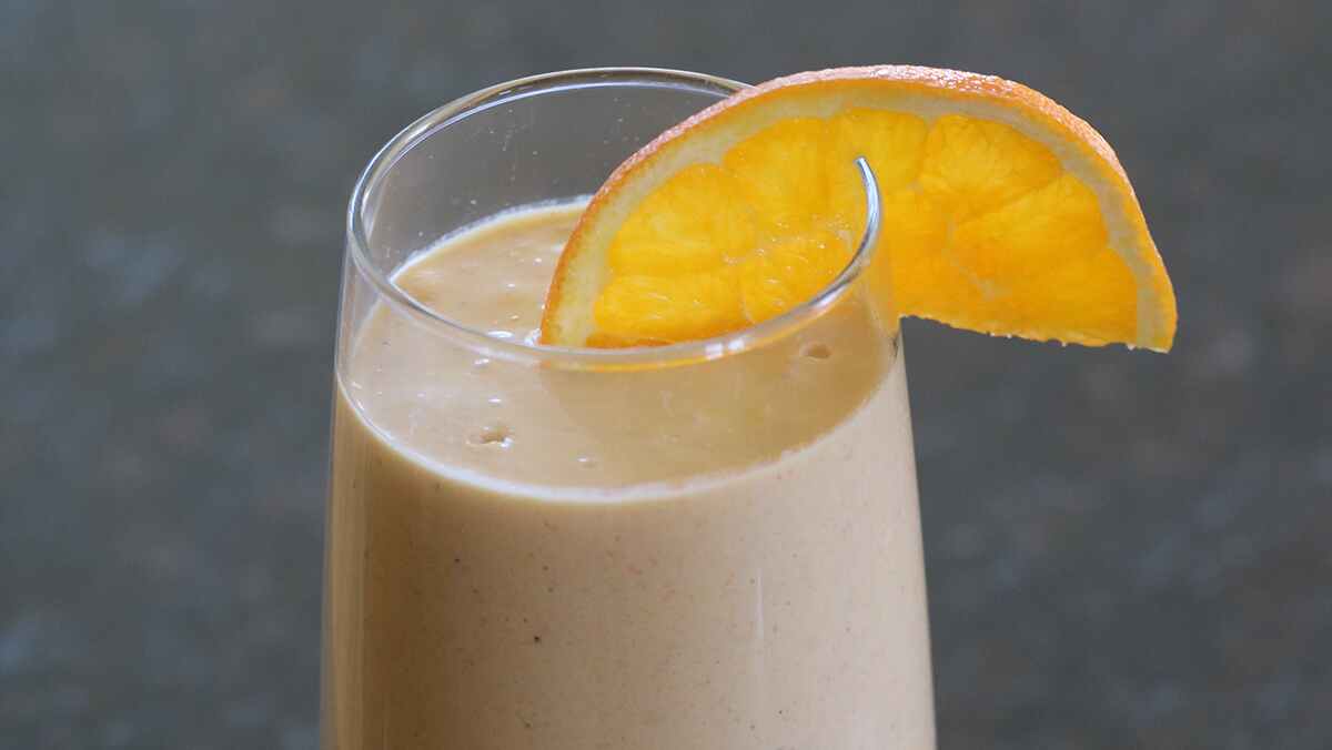 A glass with a tan opaque liquid and an orange slice on the rim