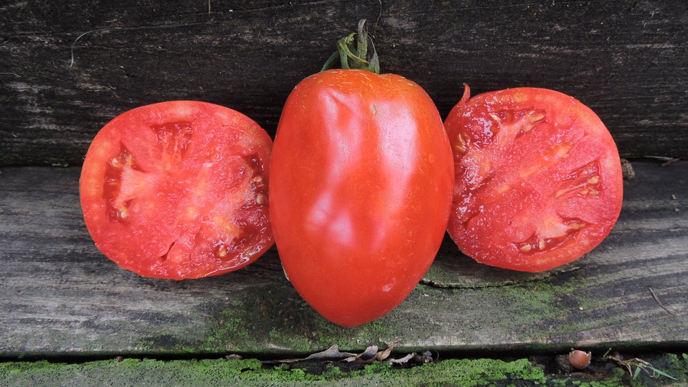 A whole tomato between two halved tomatoes on a wooden surface