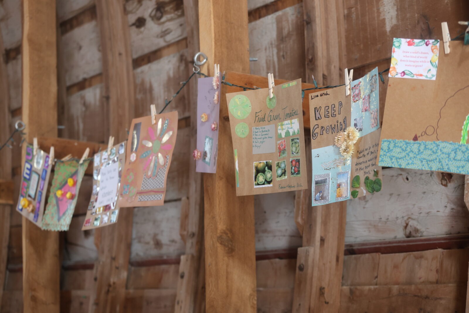 A bunch of scrapbook pages hanging on a line of string with clothespins in a barn