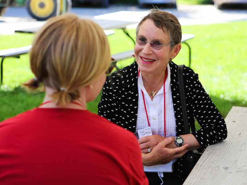 A woman in a white shirt and black and white jacket conversing with a woman in a red shirt while outdoors