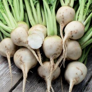 A pile of white 'Albino' beets with long green stems on a wood picnic table.