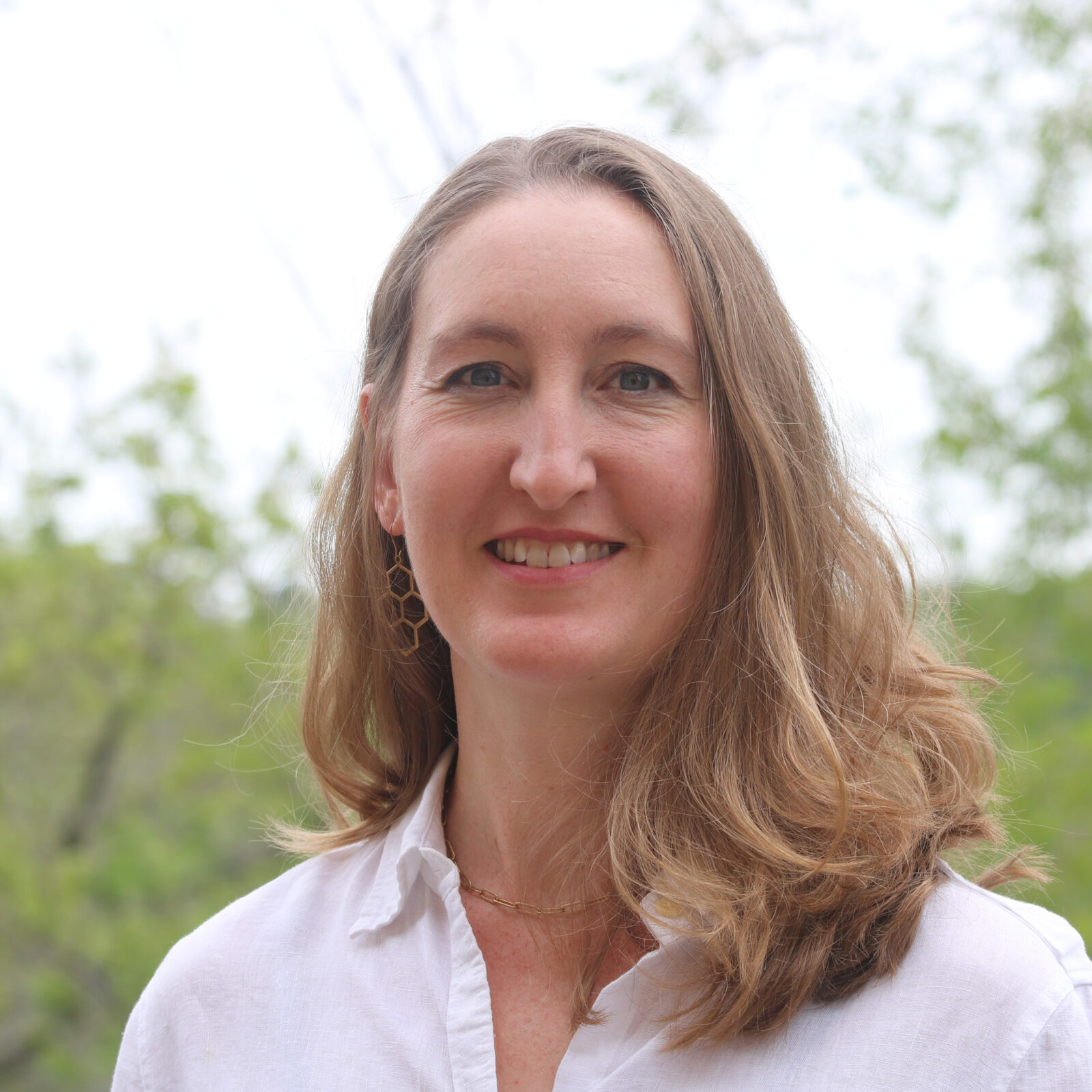 Woman with blonde hair wearing a white button-down shirt smiling into camera.