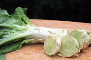 A stalk and several slices of 'Cracoviensis' celtuce on a wooden cutting board