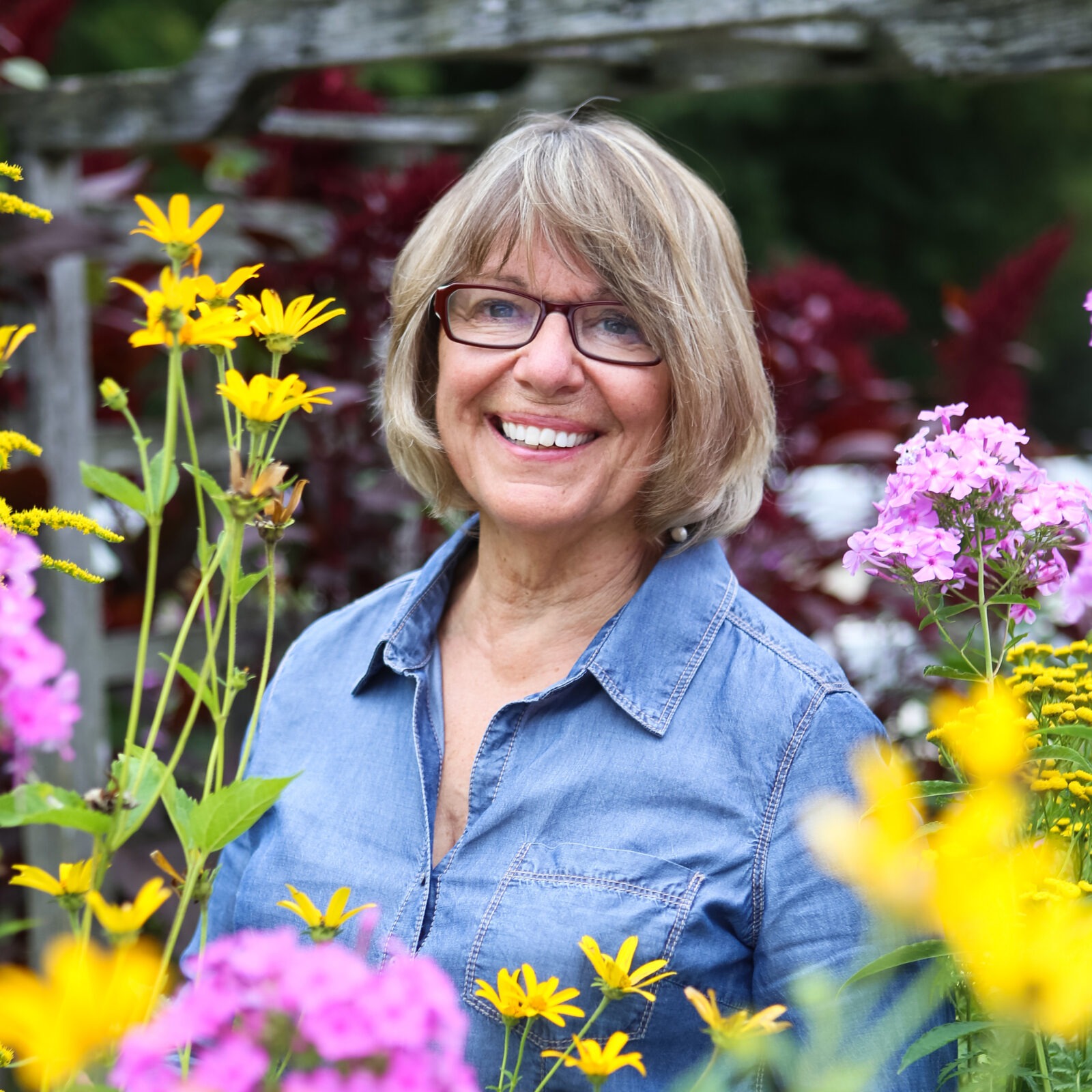 A woman smiles to camera surrounded by flowers.
