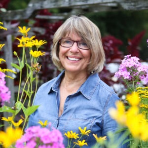 A woman smiles to camera surrounded by flowers.