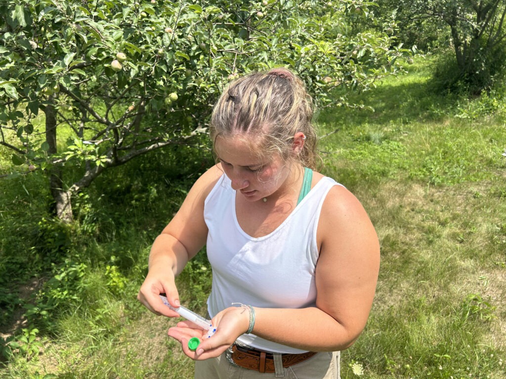 A woman stands outdoors pouring the contents of a small test tube into her hand.