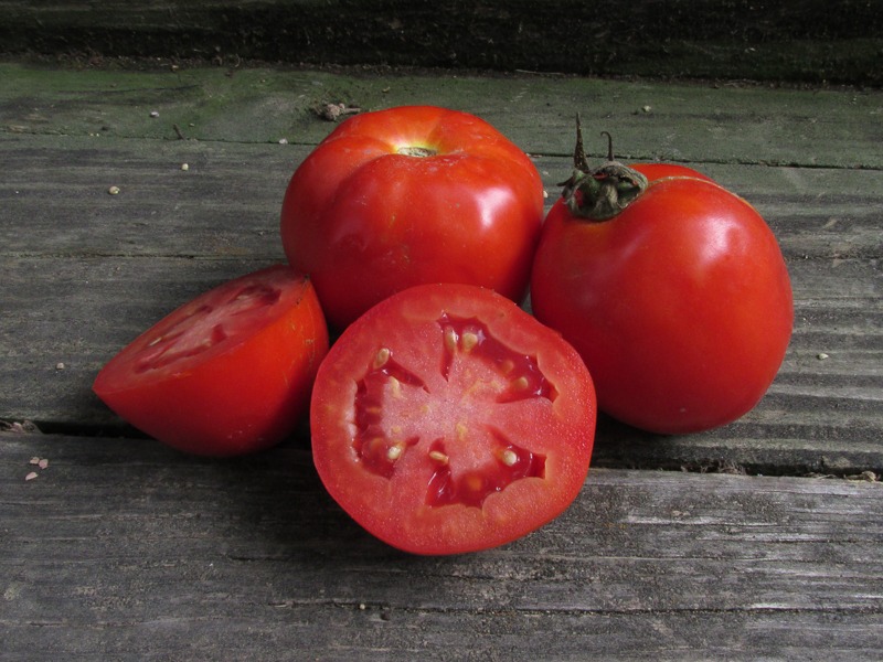 Two red tomatoes and two tomato halves on a wooden surface