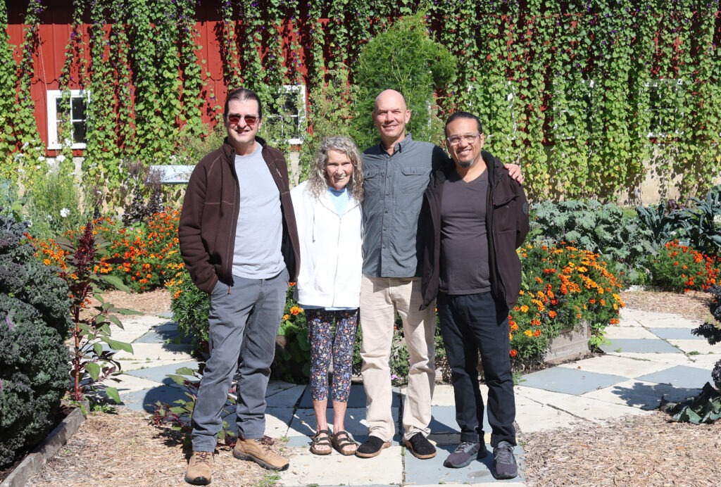 Four people pose in a garden in front of the barn at Heritage Farm