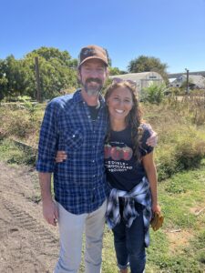 Two people smile and pose in a garden.