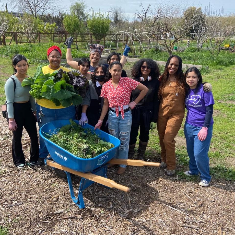 A group of middle school students pose in a garden with a wheelbarrow of collard greens.