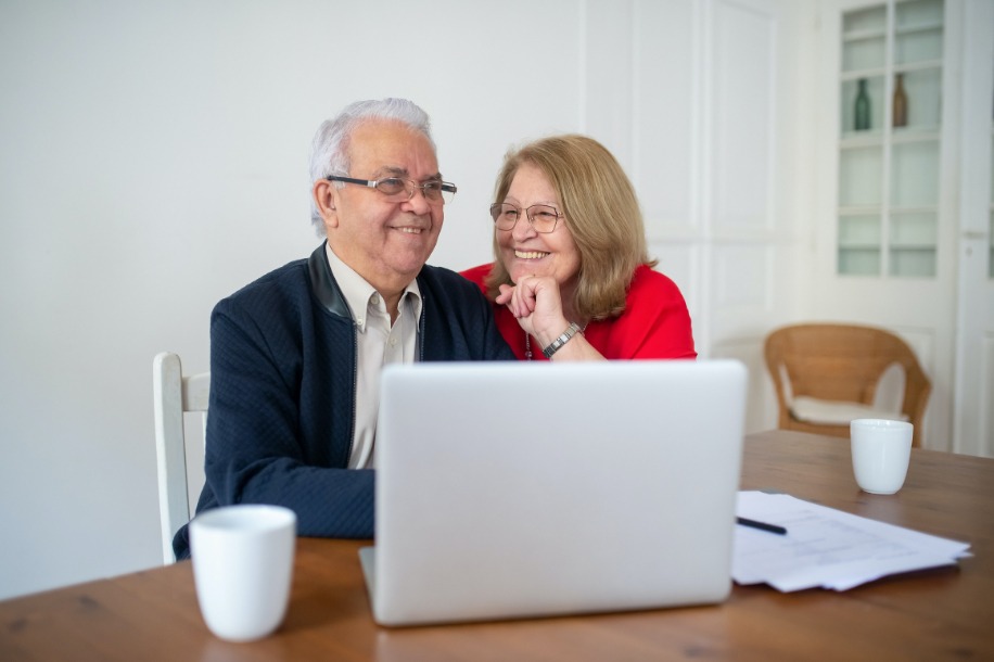 Two people sit side by side facing an open laptop.