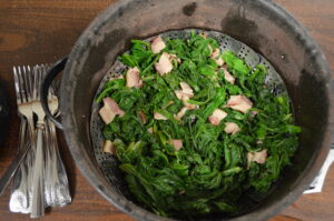A bowl of greens and bacon pieces on a table with silverware to the left
