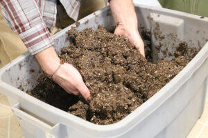 A person lifting soil out of a large bucket with their hands