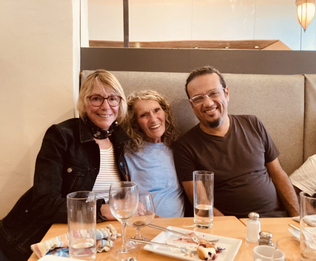 Three people sit in a restaurant booth with their arms around each other's shoulders