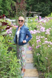 A woman poses in a garden surrounded by pink flowers.