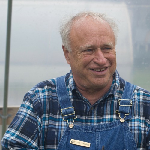 A smiling man in overalls and a blue plaid shirt