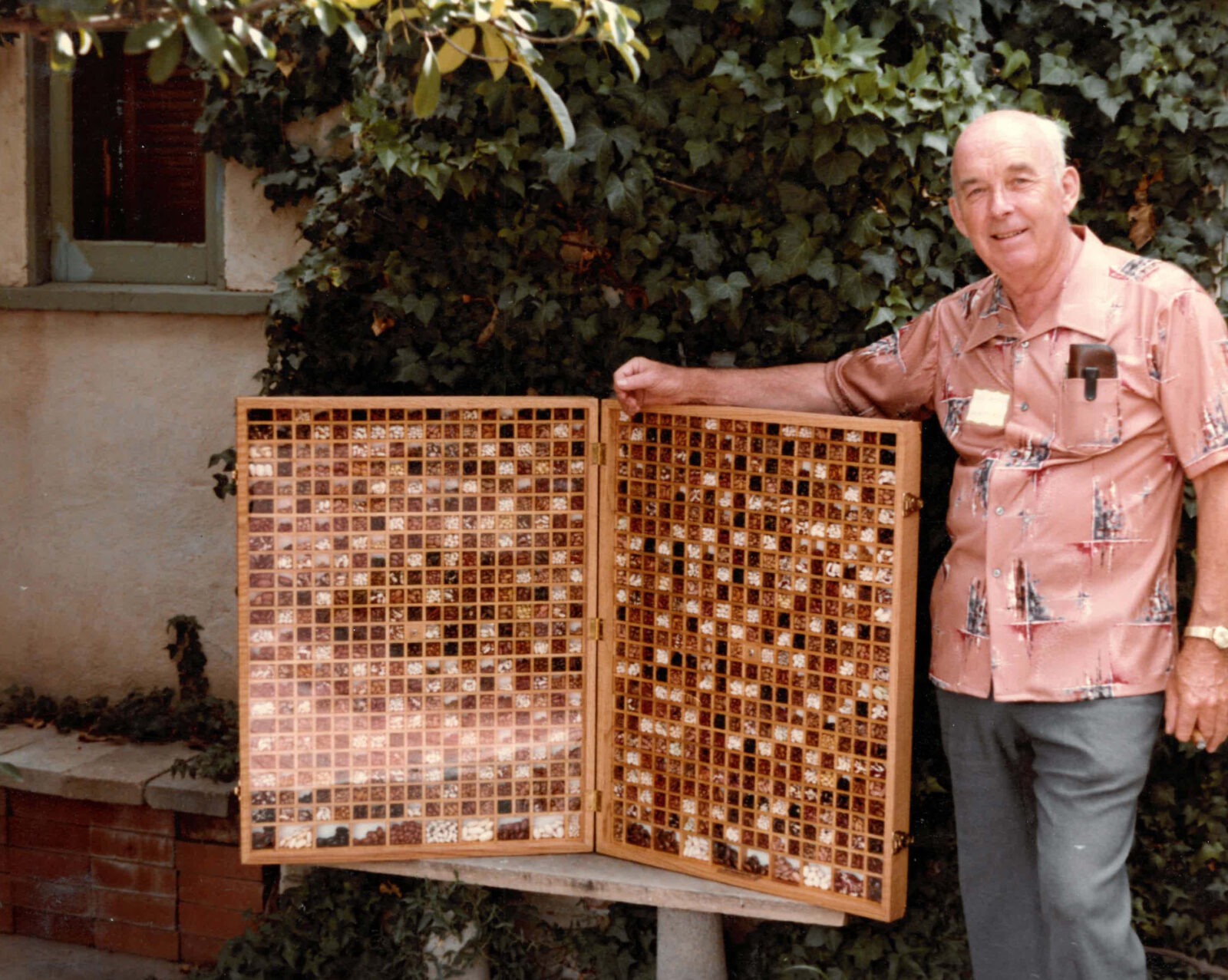 A man poses next to a large wooden case displaying hundreds of different bean varieties