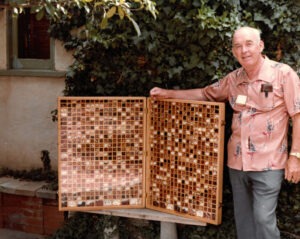 An older man poses next to a large wooden case displaying hundreds of different bean varieties