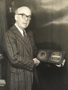 John Withee wears a striped suit holds an award