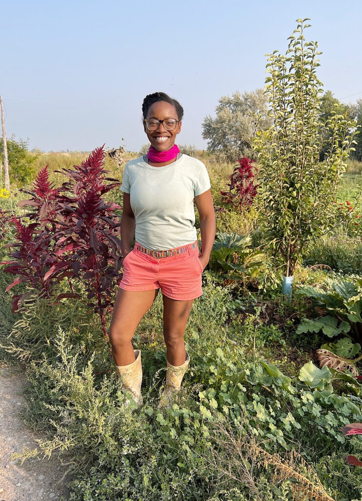 A woman stands with her hands in her pockets in a garden.
