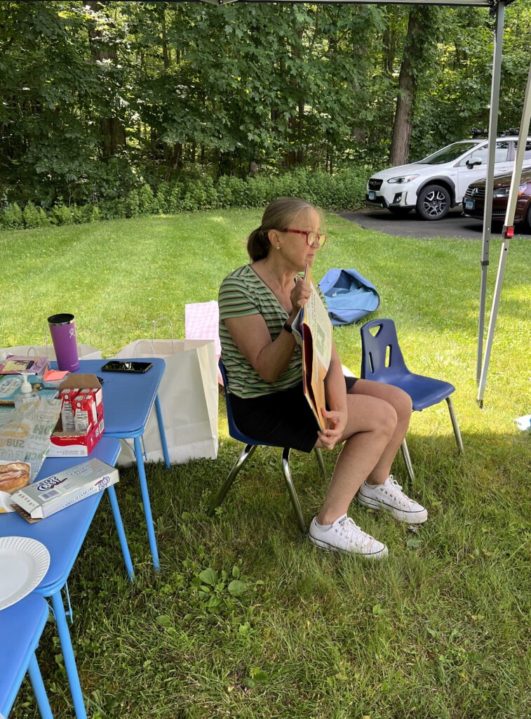 A woman sitting in a chair holding a book she is reading to an unpictured crowd.