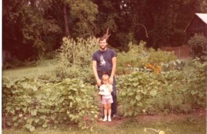 A man stands with his daughter in a garden.
