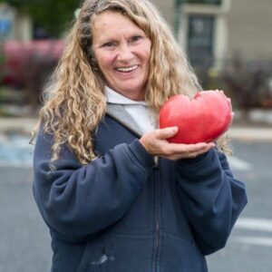 A woman smiles while holding a large red 'Peg O' My Heart' tomato