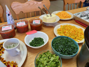 A potluck with many different baked potato toppings including salsa, butter, green onions, cheese, and more