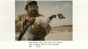 A man holds a goose in a snow-covered field with text reading: "Ron Thuma (the one with the beard) and a goose about to be banded. GKL 12/83"