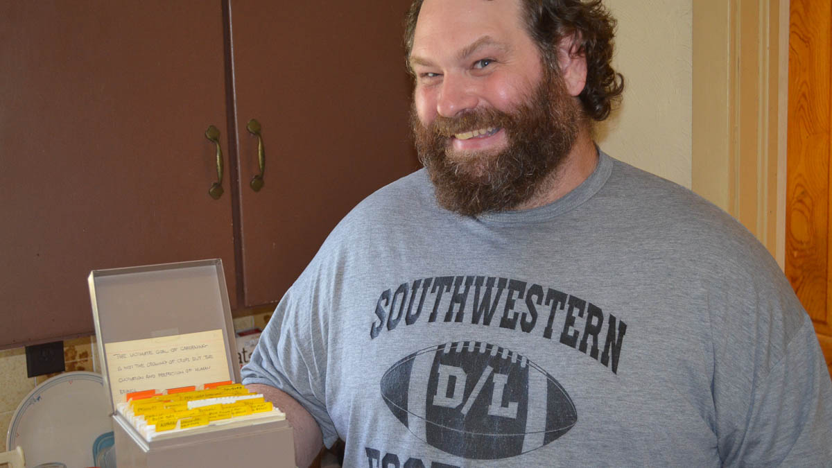 A man smiles while holding a file of index cards