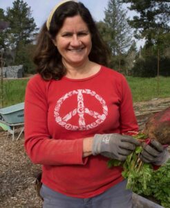 A woman in a red shirt smiles and holds a leafy vegetable in a garden