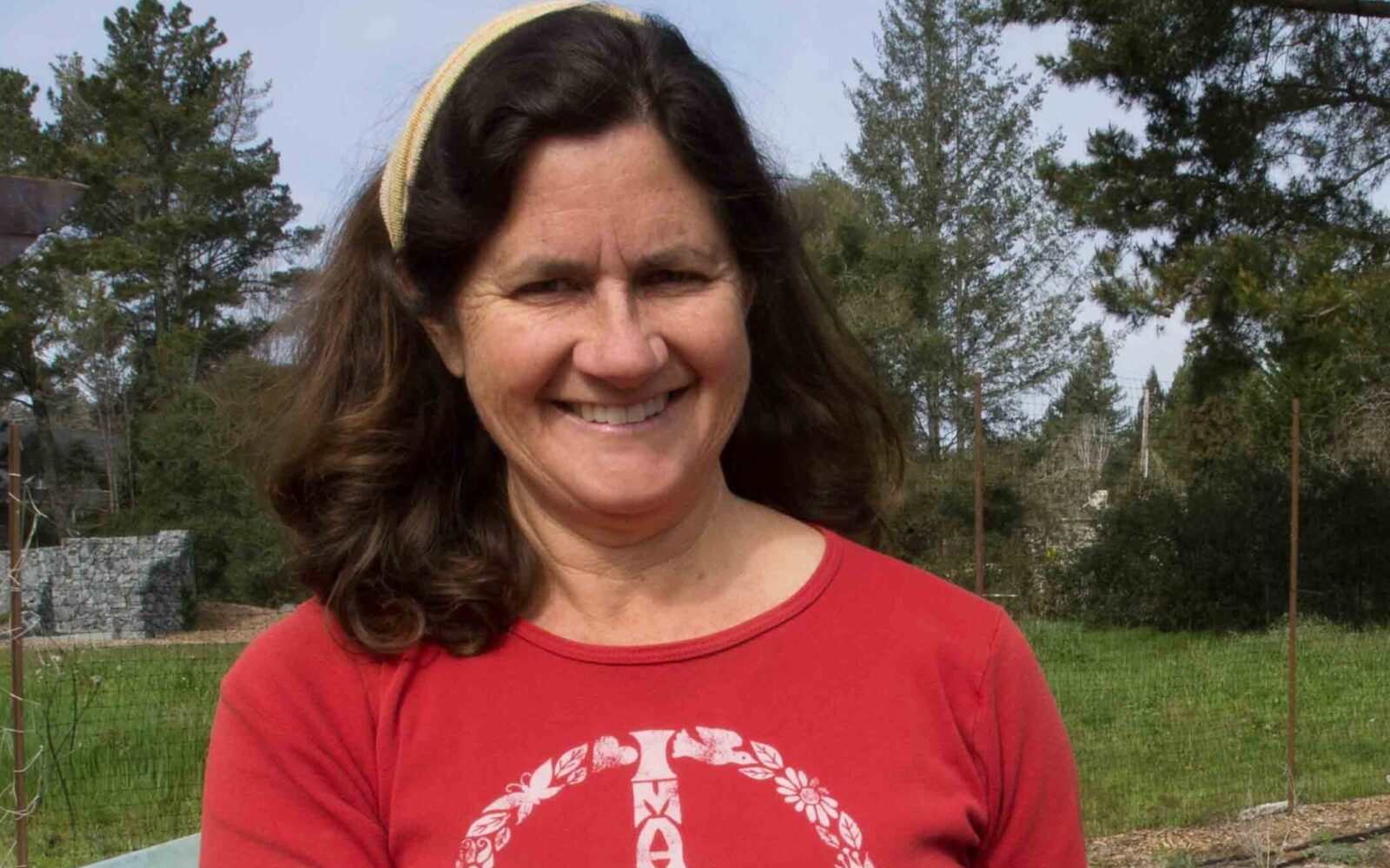 A woman in a red shirt smiles and holds a leafy vegetable in a garden