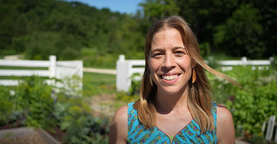 woman in sleeveless top stands in garden surrounded by white picket fence