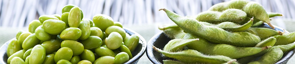 A bowl of shelled small green beans next to a bowl of green bean pods