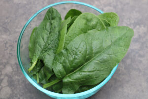 A glass bowl filled with green 'Bloomsdale' spinach leaves.