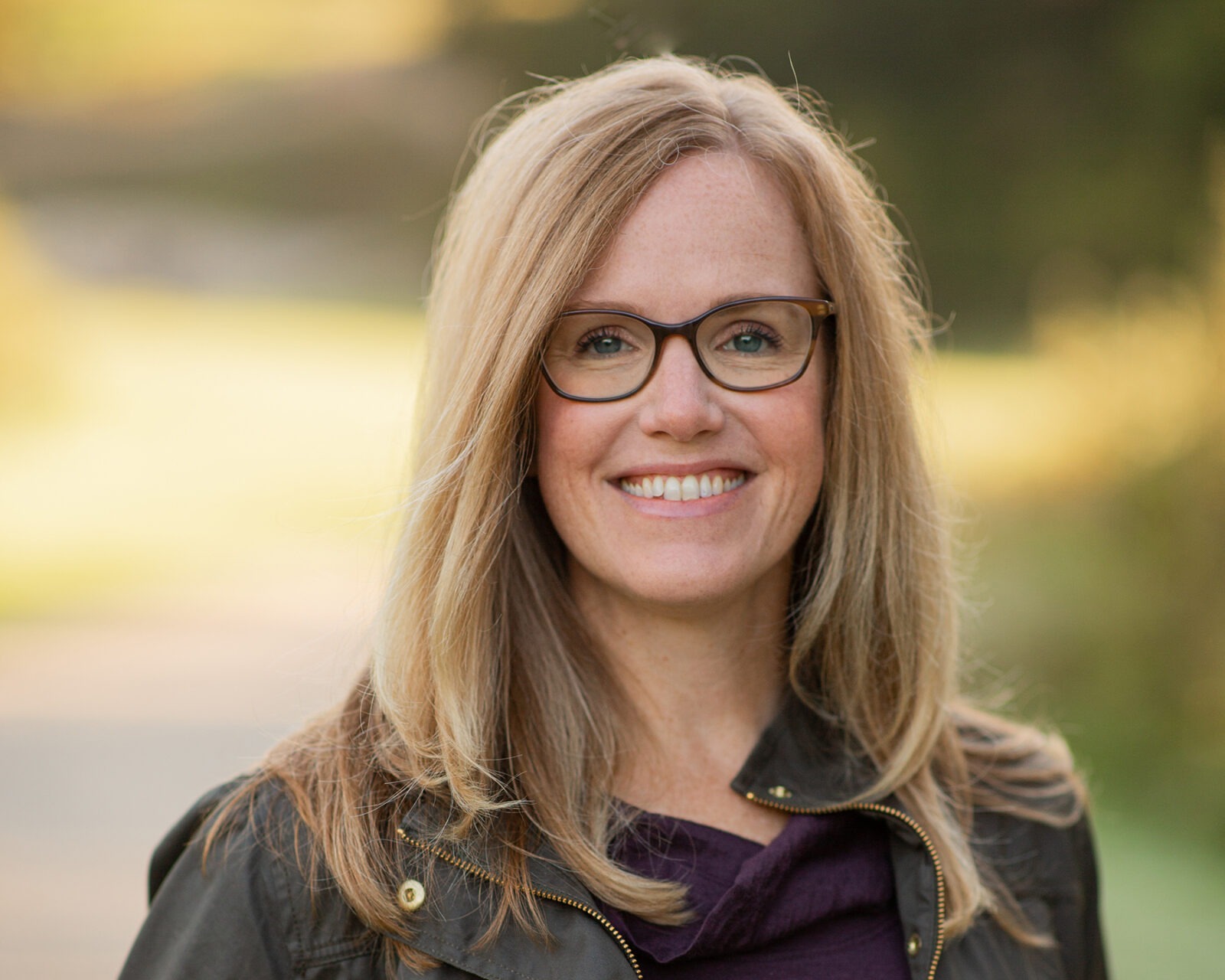 Woman with blonde hair wearing glasses smiles into camera.