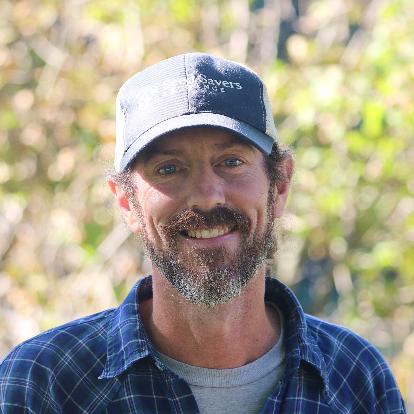Man with a beard wearing a baseball cap smiles into camera.