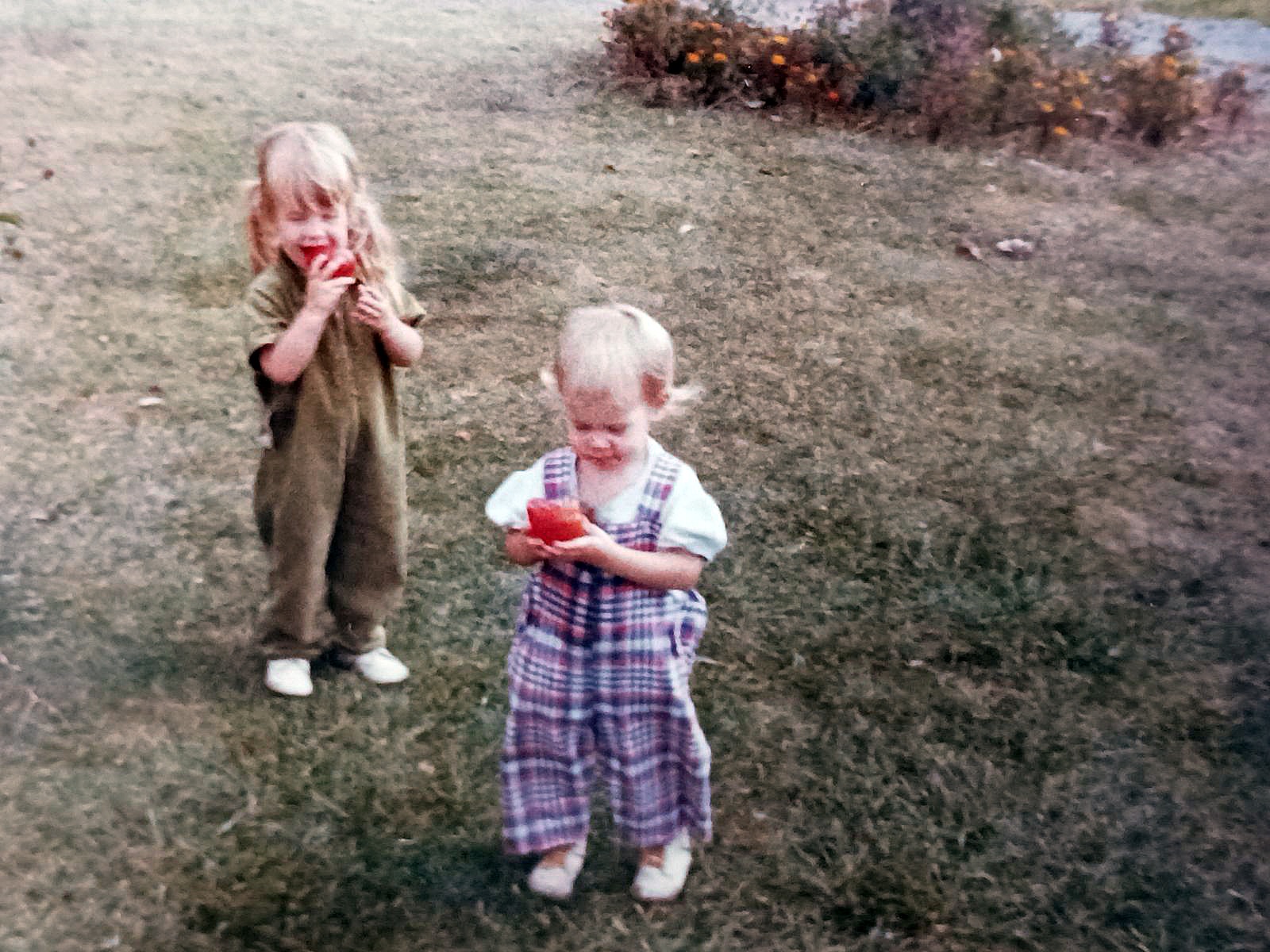 two little girls in bib overalls holding tomatoes