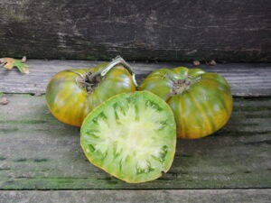 Two green and yellow 'Stoke's Green' tomatoes and one green tomato slice arranged on a wooden bench.
