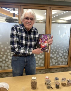 older man in plaid shirt holds a copy of the 2025 SSE Yearbook