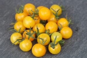 A pile of tiny round yellow tomatoes on a gray surface