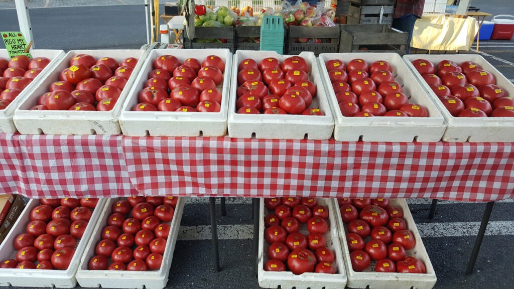 A table with containers of many large tomatoes with more containers of tomatoes underneath