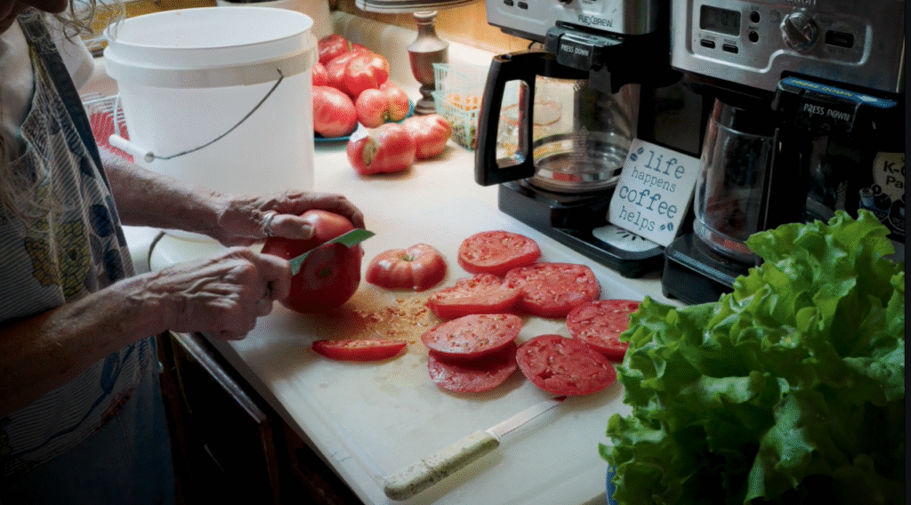 A woman slices a large 'Peg O' My Heart' tomato on a countertop in her kitchen, with more tomato slices next to her