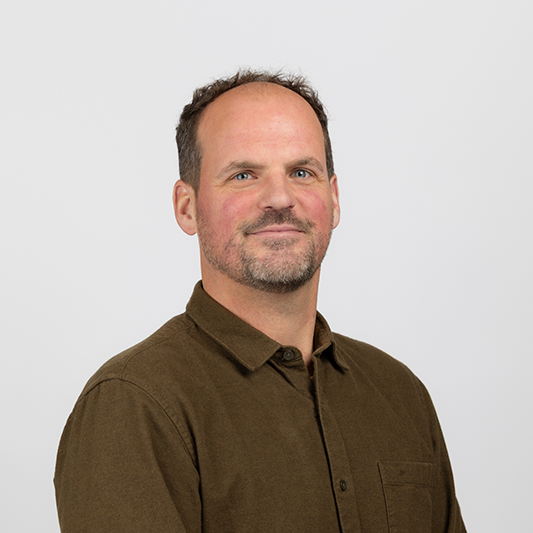 Man with a brown shirt faces the camera.
