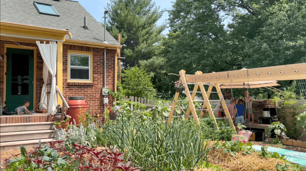 A brick house with a porch behind a garden and wooden monkey bar structure