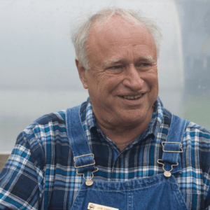 Man on overalls smiles looking off camera.