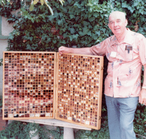 John Withee poses next to a large wooden case displaying hundreds of different bean varieties