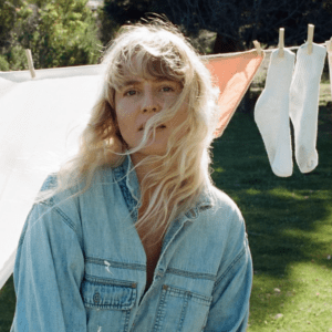 A woman with blonde hair blowing in her face looks into camera. 
