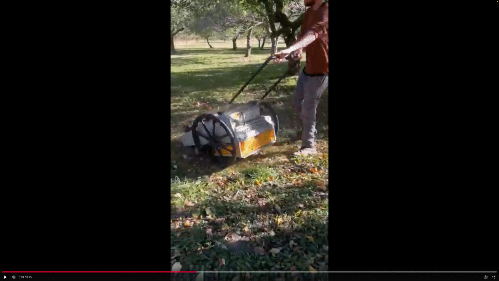 A person pushes a machine that picks up fallen apples in an orchard