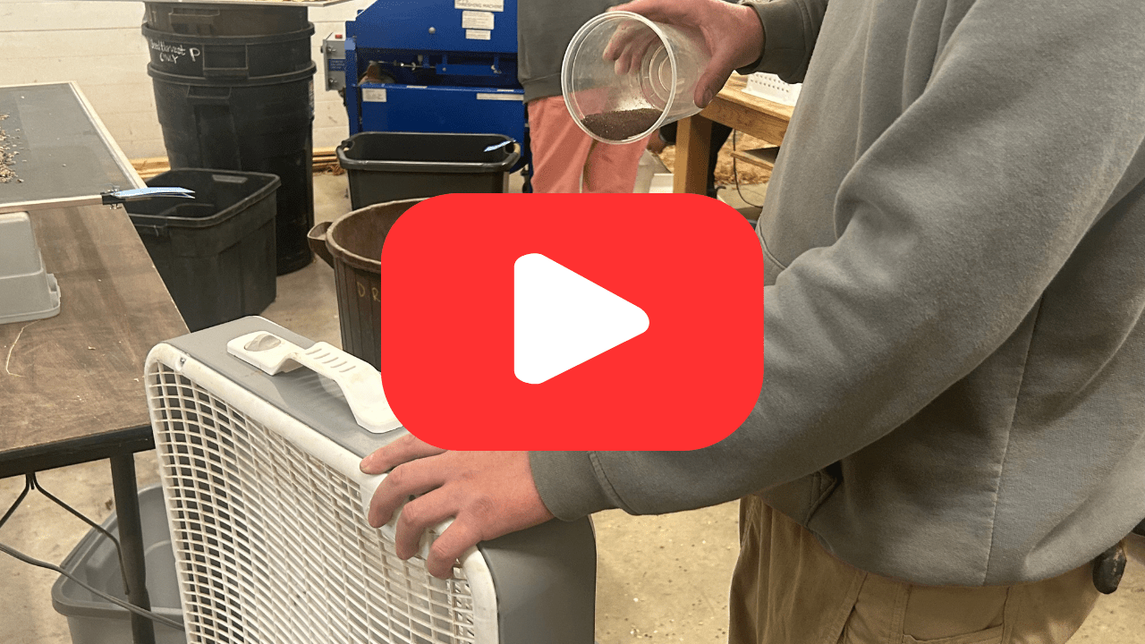 A person in a gray sweatshirt reverse winnows petunia seeds in front of a box fan